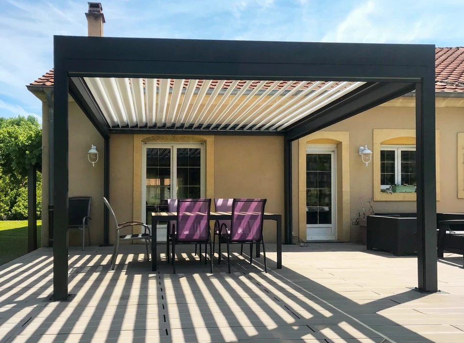 Terrasse extérieure équipée d'une pergola bioclimatique à lames orientables en aluminium anthracite, fixée en applique sur façade enduite ocre