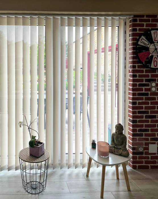 Intérieur lumineux avec store à lames verticales en tissu crème couvrant une grande baie vitrée