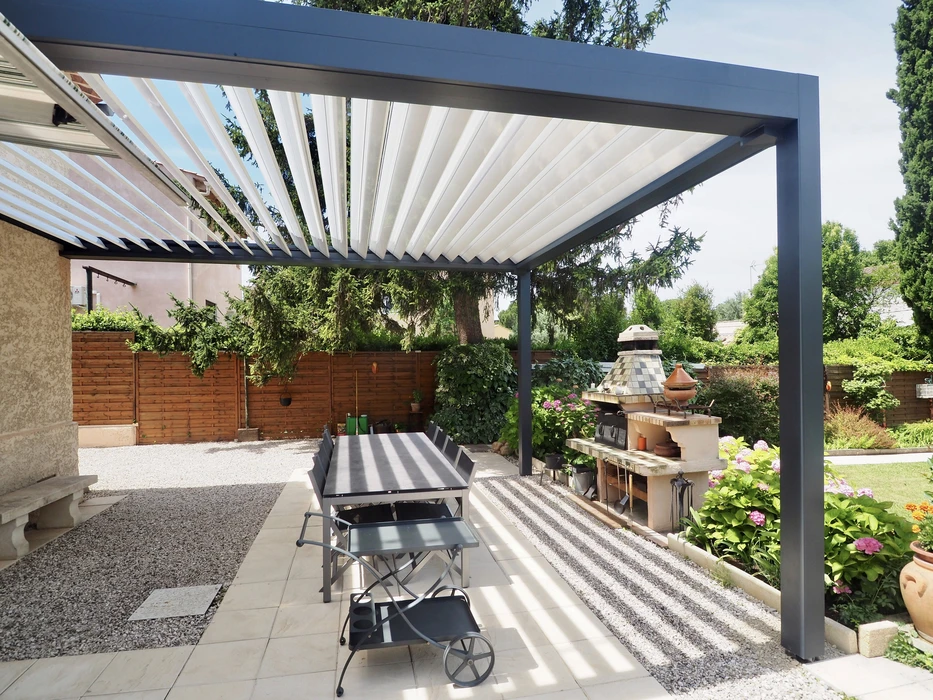 Terrasse extérieure aménagée sous pergola bioclimatique à lames orientables blanches et structure métallique anthracite