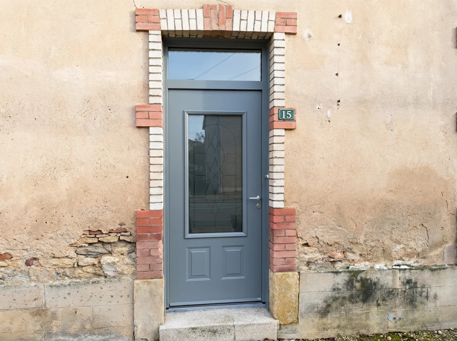 Façade ancienne en crépi beige dégradé avec encadrement en briques rouges et blanches