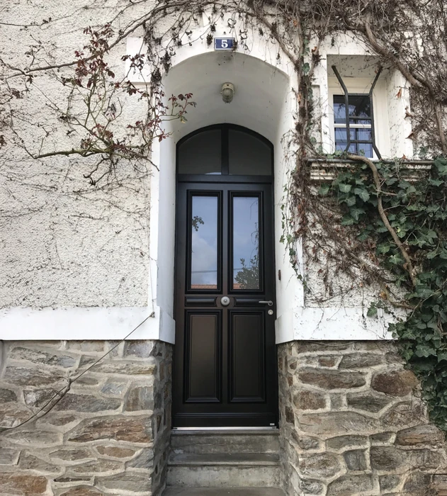 Entrée résidentielle avec porte noire à panneaux vitrés sous arche blanche