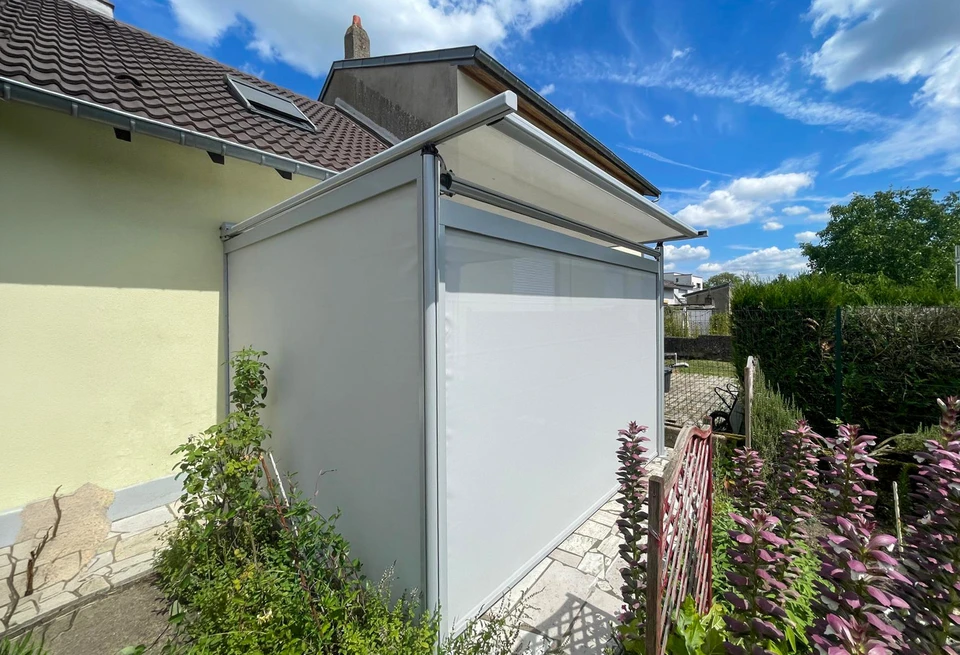 Un professionnel menuisier-vendeur présentant des échantillons de stores extérieurs à un couple de clients devant une baie vitrée d'une maison. Le professionnel tient des nuanciers ou des modèles de stores, pointant vers une installation de store extérieur visible sur la façade. L'atmosphère doit être professionnelle et bienveillante, montrant clairement l'interaction client-prestataire dans un contexte résidentiel de menuiserie extérieure.