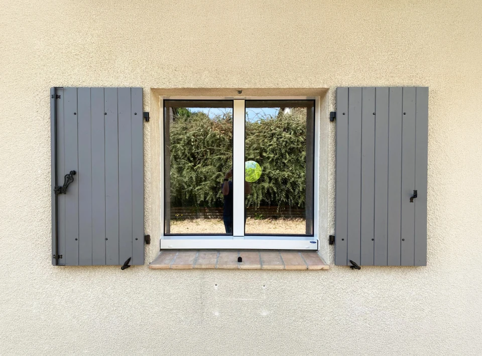 Façade extérieure d'habitation avec fenêtre à deux vantaux et volets battants en aluminium gris